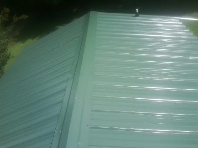 New green metal panels meeting at the ridge of a roof — Flat Roof Repair work by our crew in Forest Park