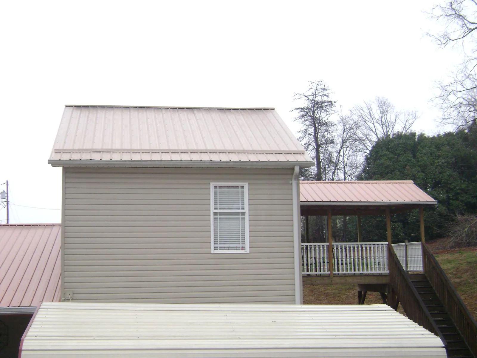 Tan metal roofs on a two story addition and attached porch, from a Roof Replacement job in Forest Park